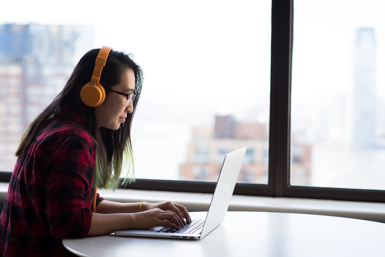 Asian woman with headphones using laptop for remote work in a city setting.